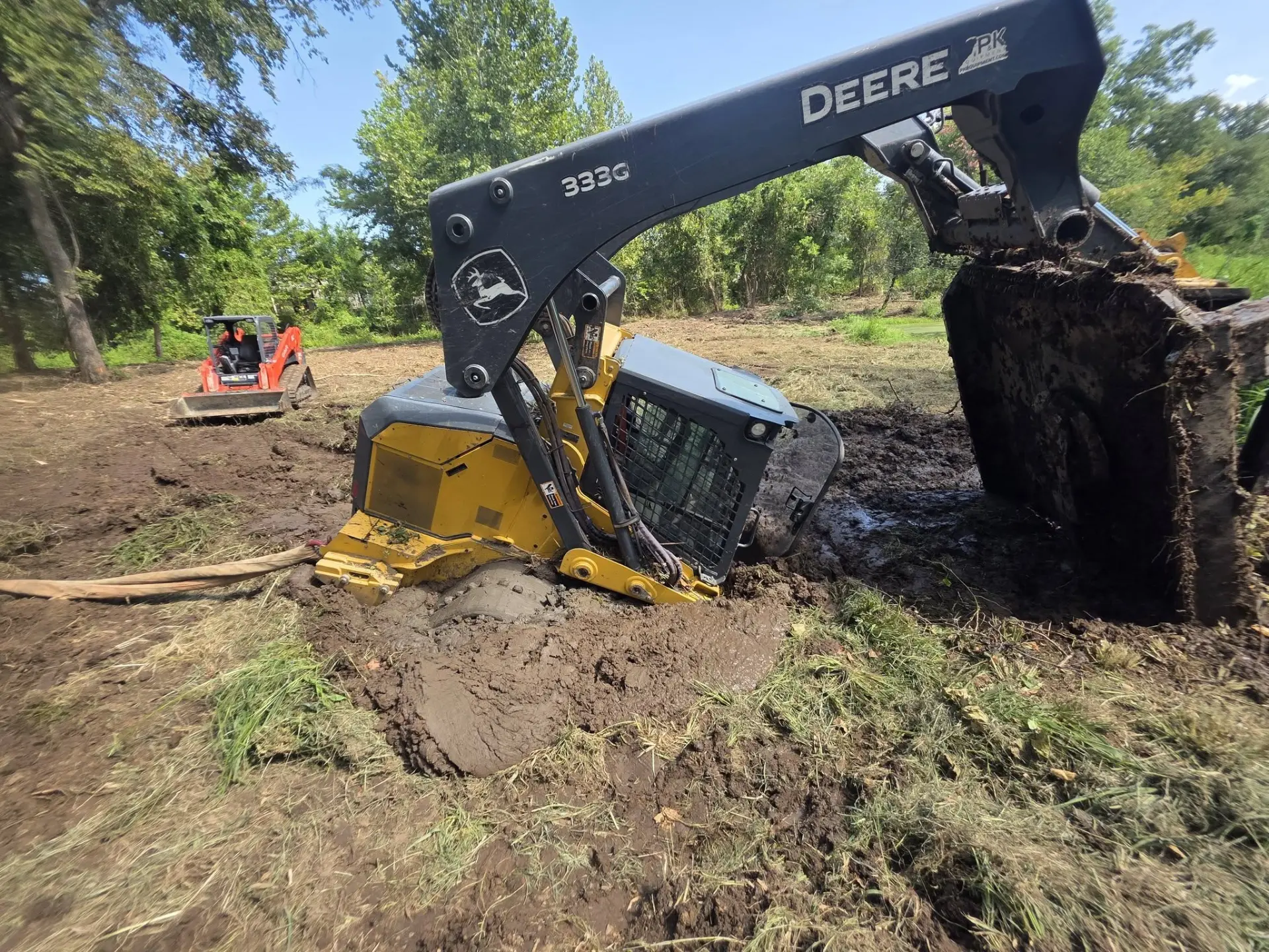 John Deere 333G track loader working deep soft ground on a pond area
