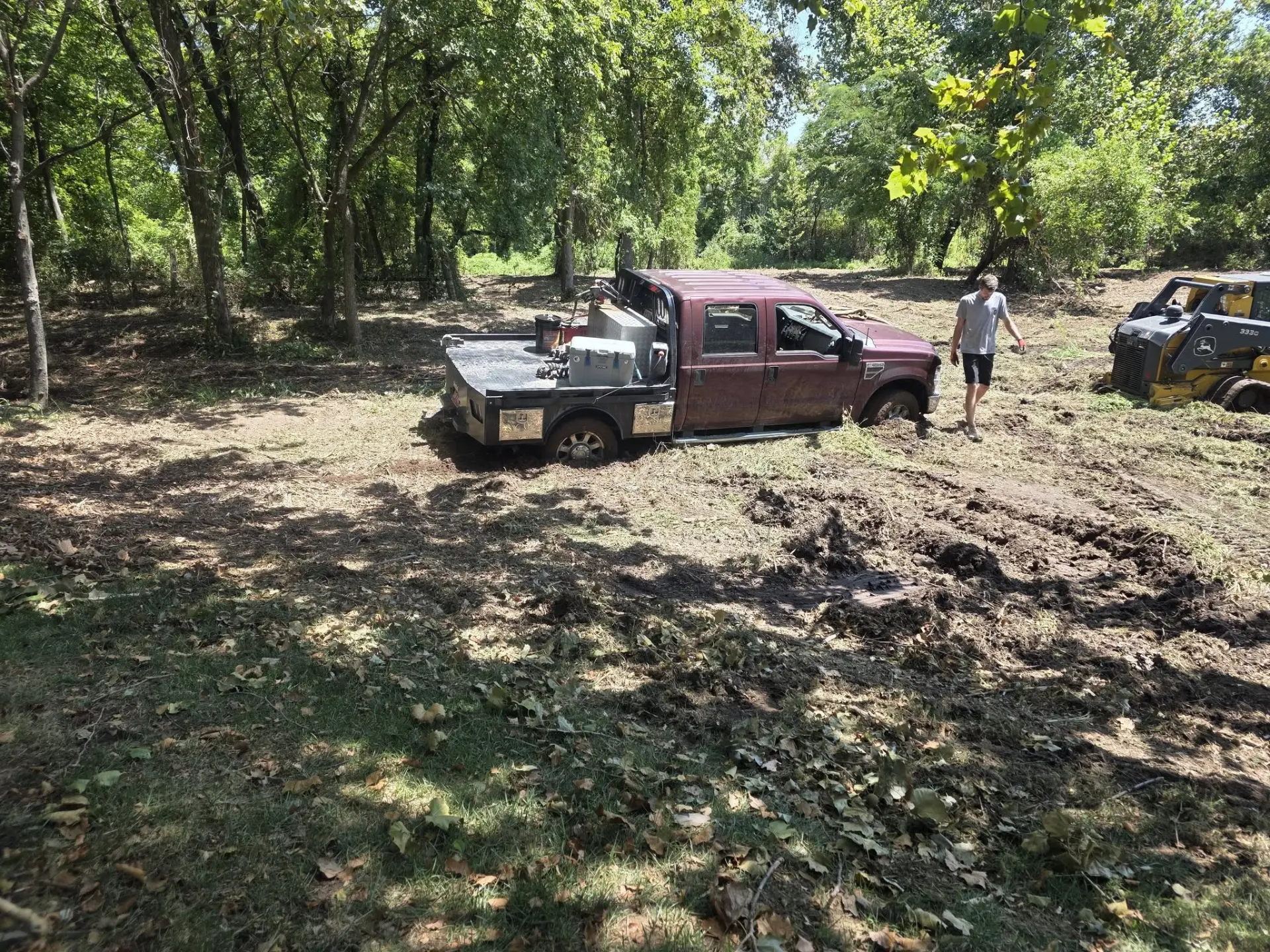 Work truck and skid steer on a cleared job site under pecan trees